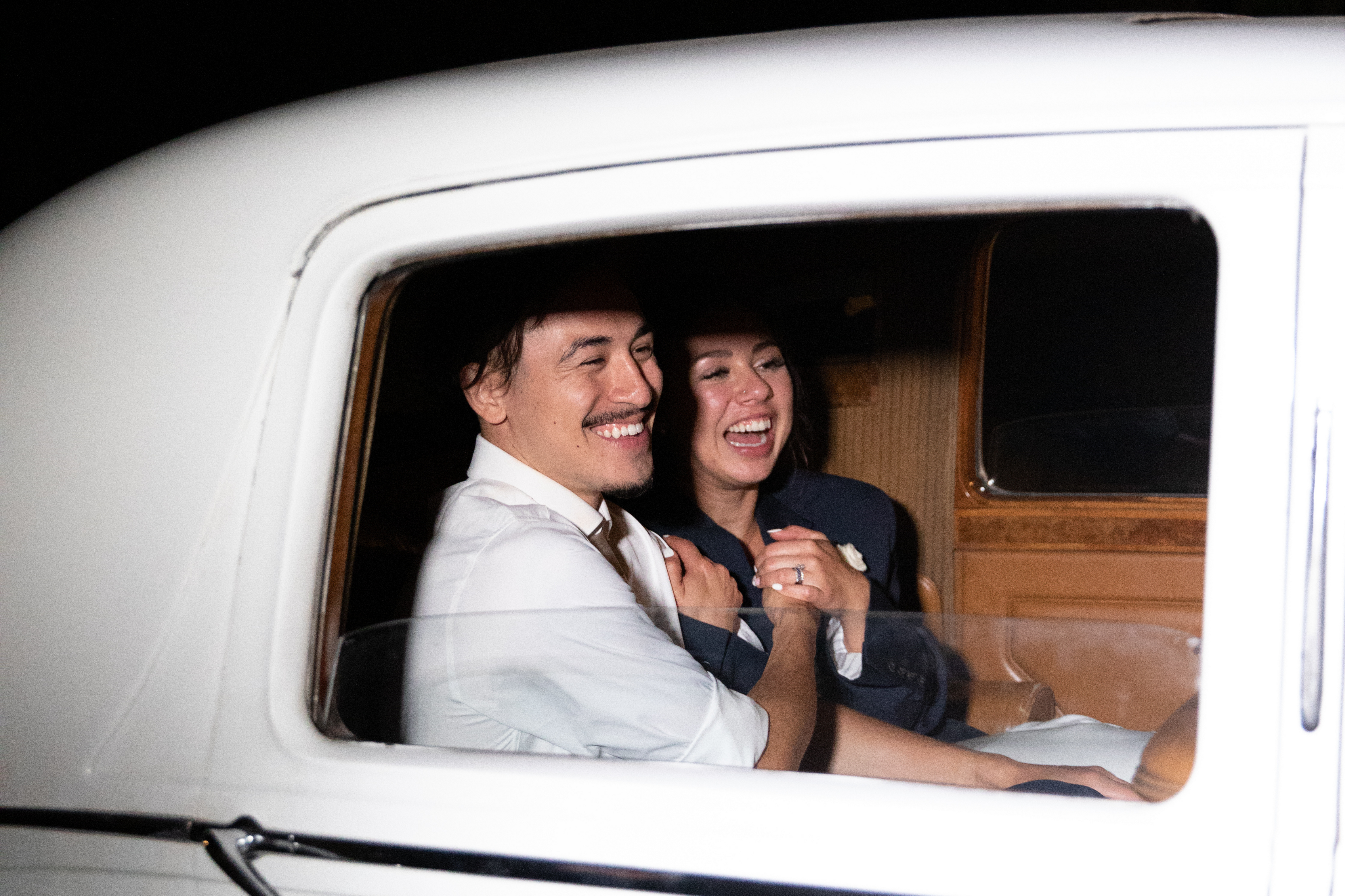 Wedding Bride and Groom Smiling at Send Off In Vintage White Car Holding Hands