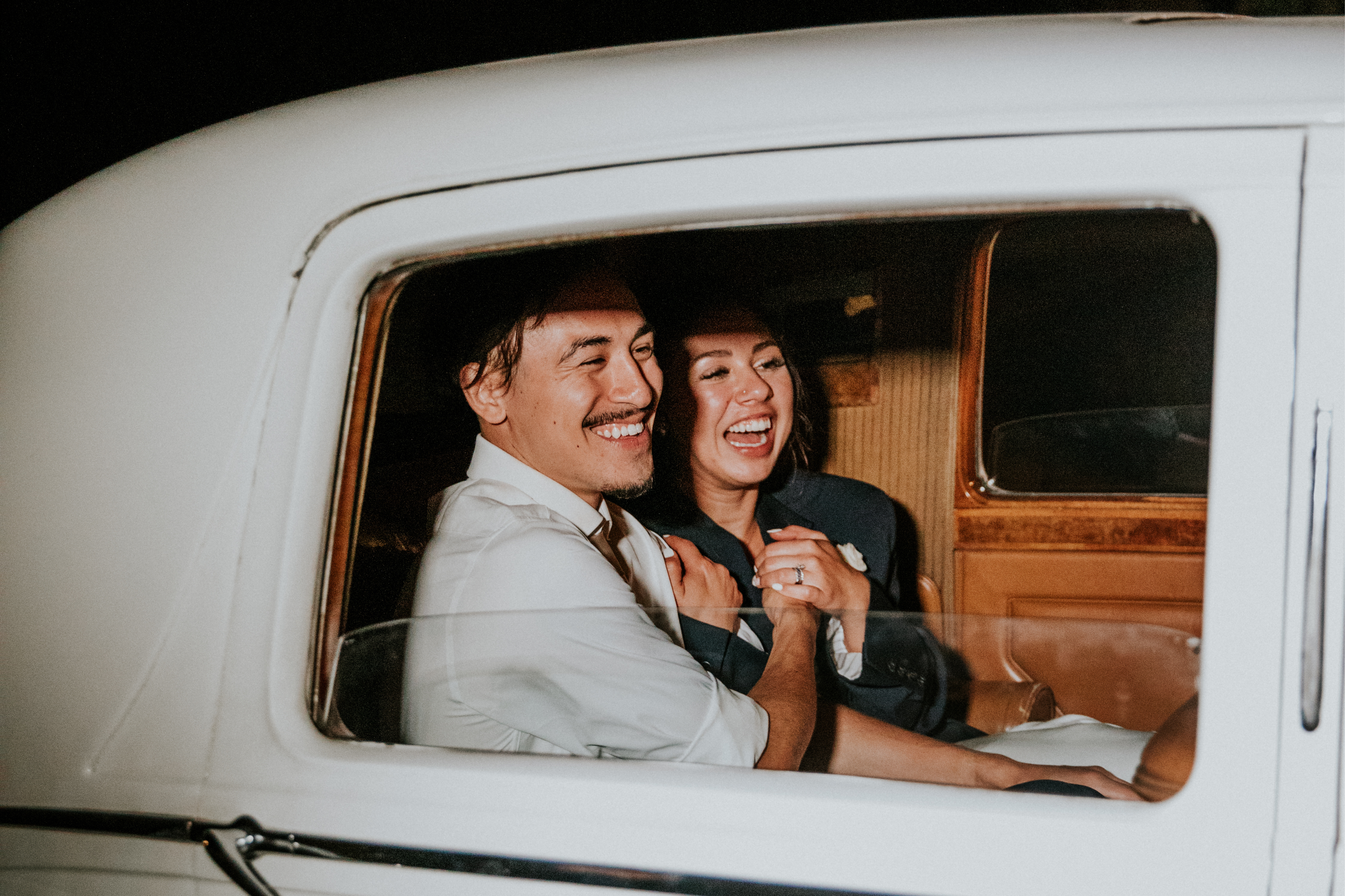Wedding Bride and Groom Smiling at Send Off In Vintage White Car Holding Hands